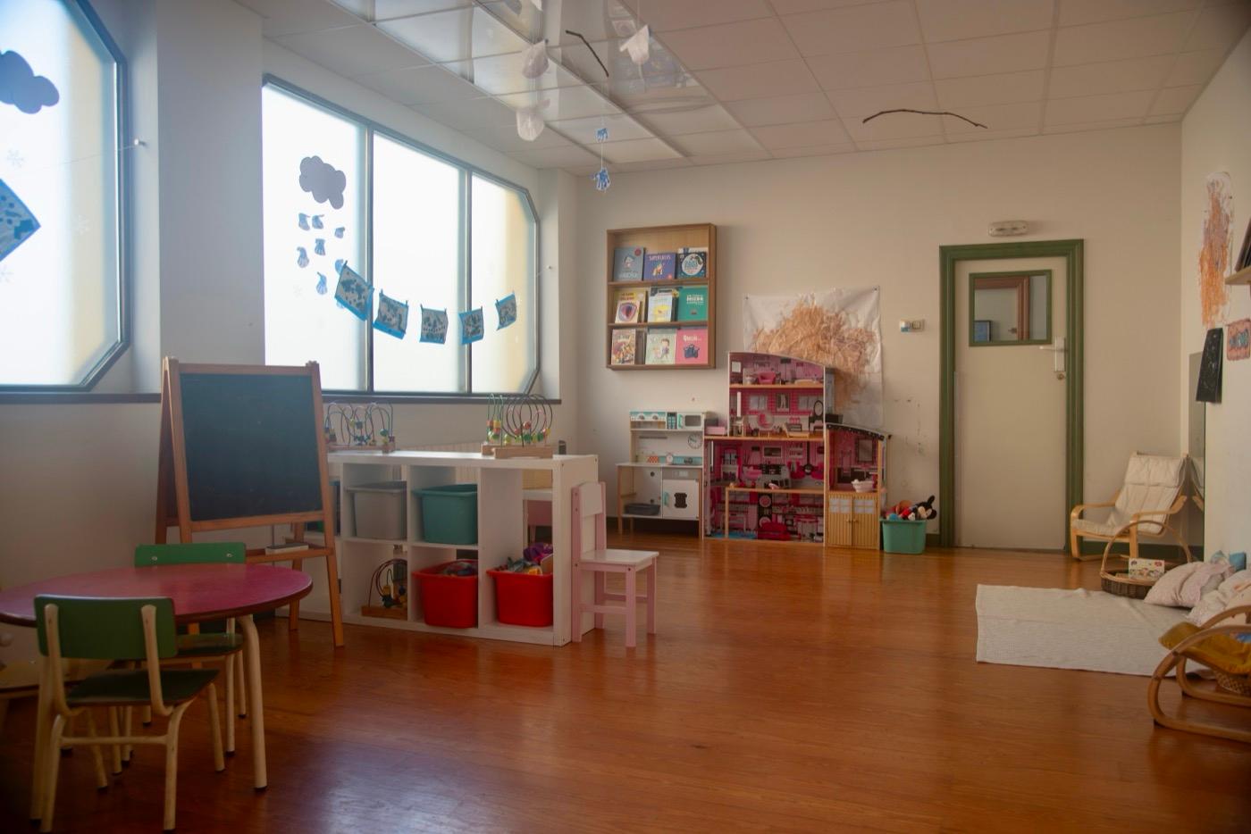 Aula de 2 a 3 años con la casita de muñecas, la pizarra y las mesas