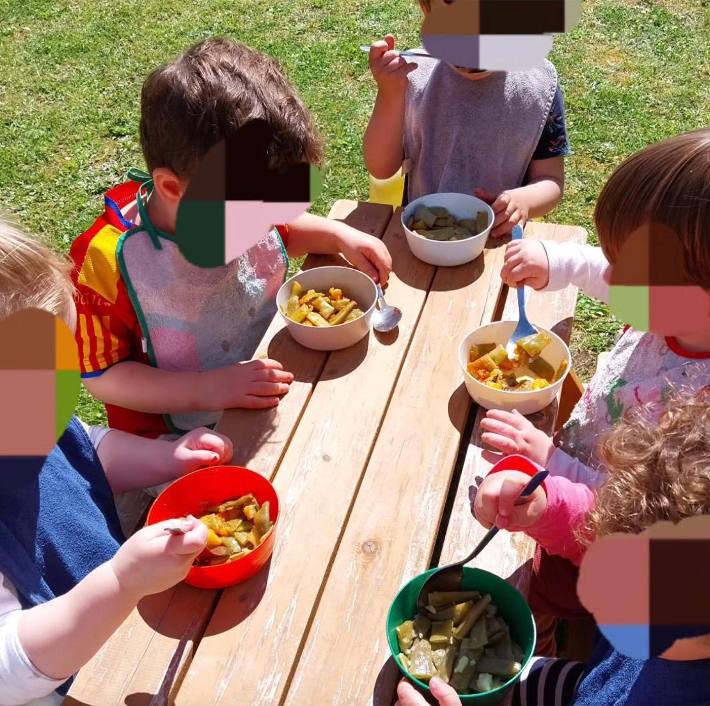 Niños comiendo en la mesa de madera del patio, con baberos